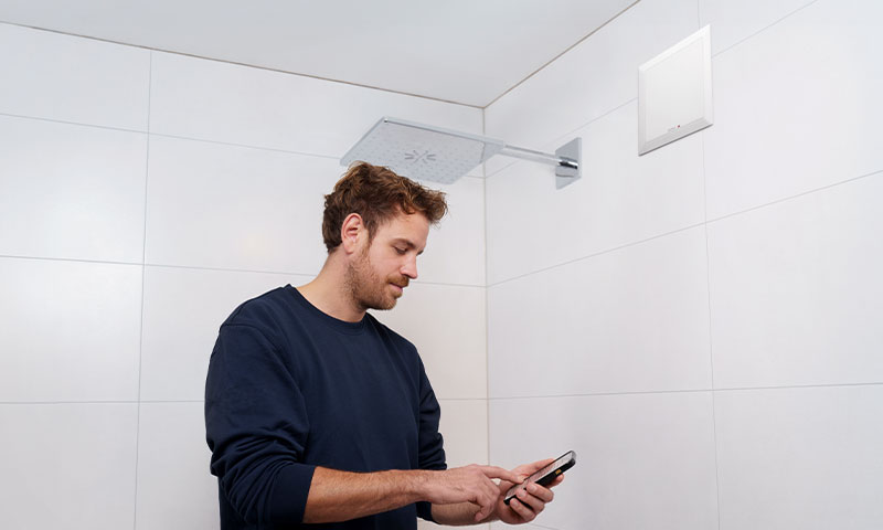 Installateur steht im Smartphone in einer weißen Duschen, ELS NFC an der Wand